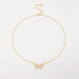 A delicate 18K gold plated cable chain necklace featuring a sparkling cubic zirconia ribbon bow pendant, laid flat against a white surface.