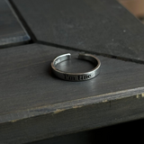 A silver "I'm fine" hidden message ring resting elegantly on a dark, rustic wooden table.