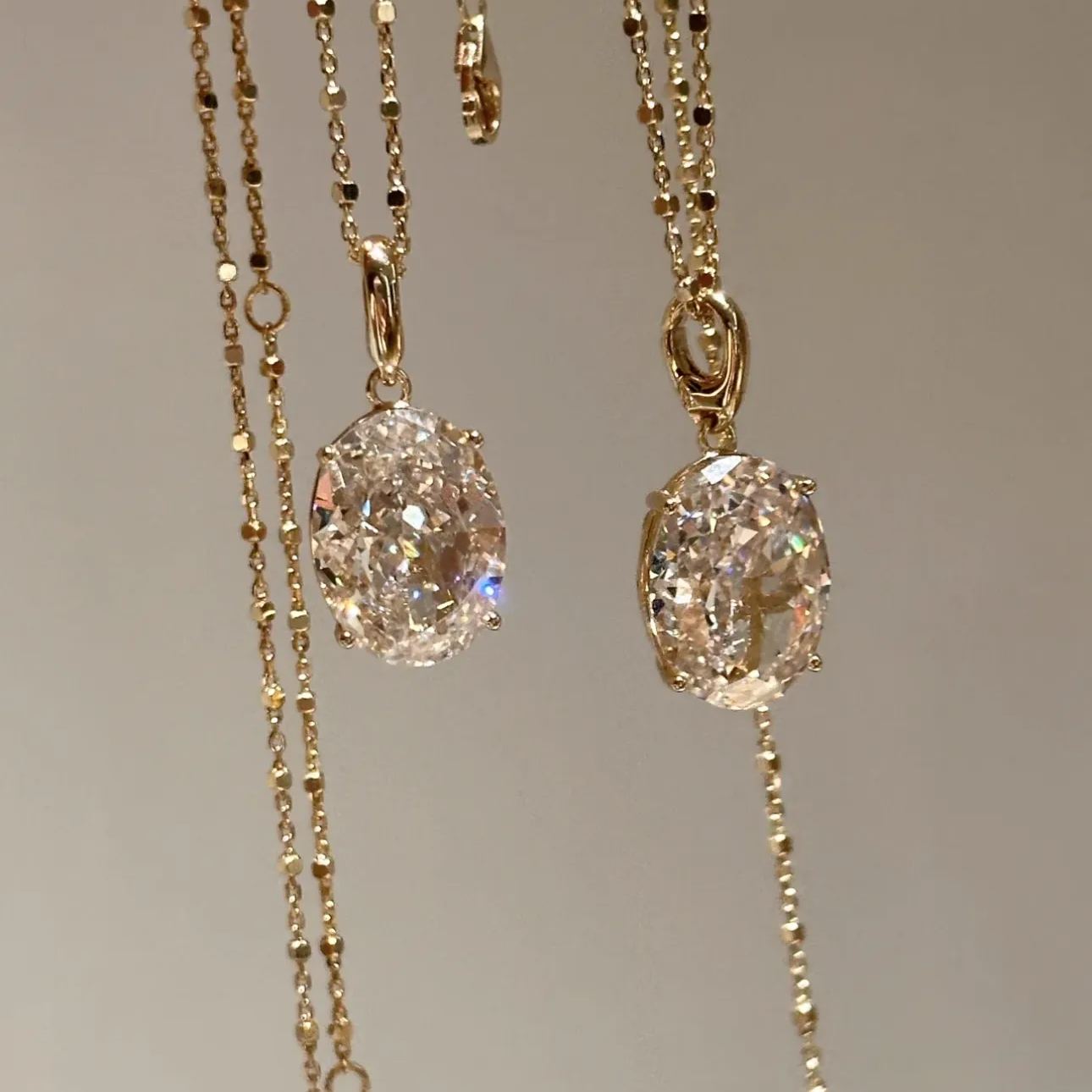 Front view of two dazzling 10 carat oval high-carbon diamond necklaces hanging side by side, reflecting pure light.
