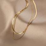 Flat lay of the 18K gold plated Snake Chain Duo Necklace resting elegantly on smooth champagne silk