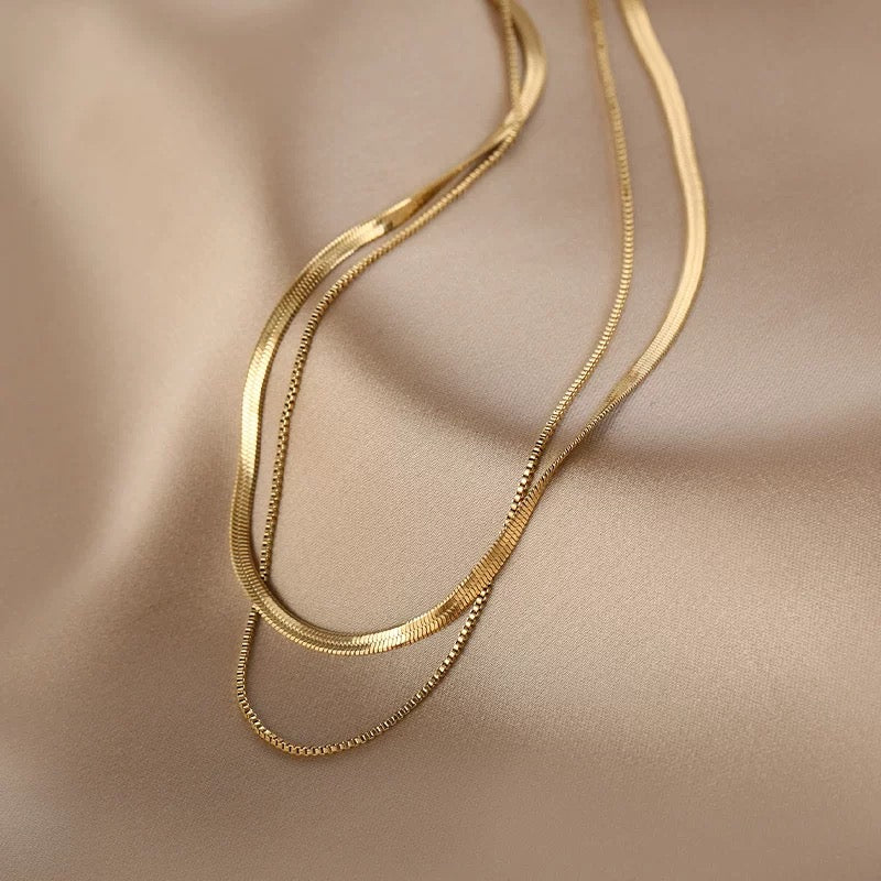 Flat lay of the 18K gold plated Snake Chain Duo Necklace resting elegantly on smooth champagne silk