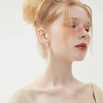 Close-up of an elegant woman modeling a waterproof gold titanium steel hoop earring with intricate pearl details.