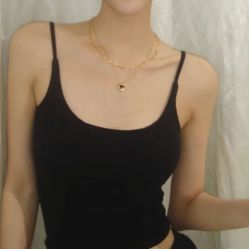 Front view of a layered gold necklace featuring a trendy paperclip choker and a small black heart pendant on a model