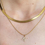 Macro detail shot on a model's neck, clearly showing the woven liquid-like texture of a gold herringbone snake chain paired with a cubic zirconia pave initial H pendant.