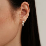 Macro detail shot of a silver 3-stone huggie hoop earring on an ear, emphasizing the shared-prong setting and stone clarity.