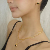Detailed view of a model wearing matching black heart jewelry, including a layered necklace and dainty heart-shaped stud earrings.