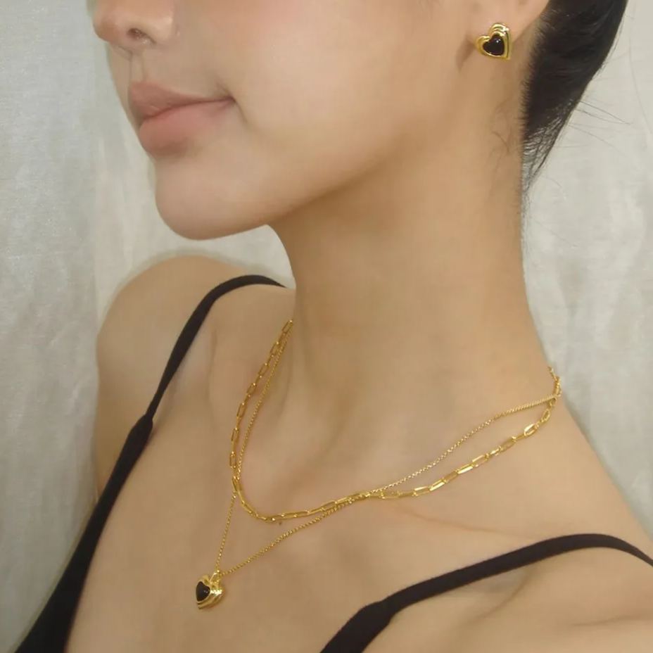 Detailed view of a model wearing matching black heart jewelry, including a layered necklace and dainty heart-shaped stud earrings.