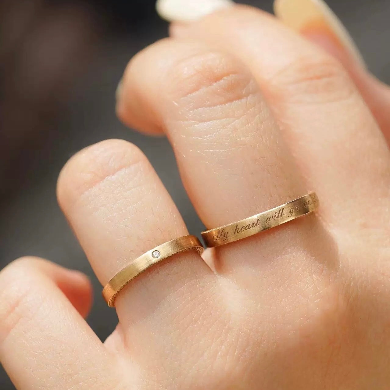 A couple wearing matching 18K gold-plated adjustable rings, featuring a custom engraved women's band reading "My heart will go on" and a single-stone men's band.