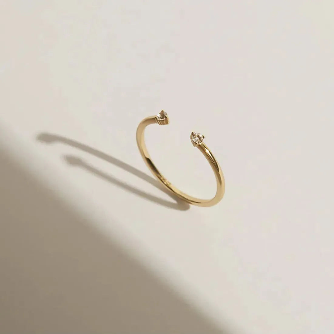 An artistic product photograph of a gold open cuff ring on a clean surface with elegant geometric shadows.