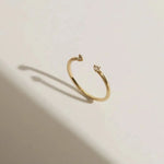 An artistic product photograph of a gold open cuff ring on a clean surface with elegant geometric shadows.