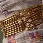 A stack of multiple elegant 18K gold-plated open cuff bangles with small sparkling solitaire diamonds, showcasing a layerable jewelry trend.
