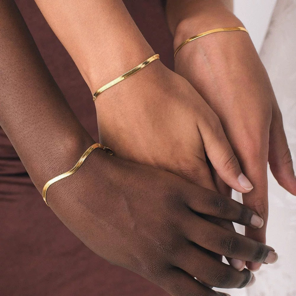 Three people with different skin tones stacking gold herringbone bracelets, showcasing inclusive beauty and jewelry trends.