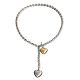 A mixed metal lariat necklace with a chunky silver chain, front toggle clasp, and two dangling puffy hearts in silver and gold, isolated on a white background.