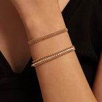 A woman's arm wearing a black top, showcasing a curated wrist stack featuring a triple-row beaded CZ bracelet paired with a thicker gold herringbone chain bracelet.