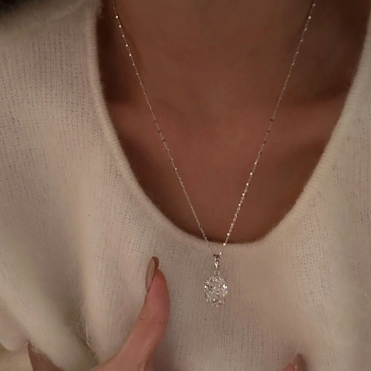 A woman in a cozy white sweater wearing the breathtaking 10 carat oval silver pendant necklace on her collarbone.