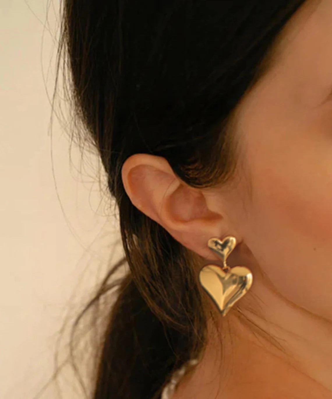 Close-up of a woman wearing 18K gold plated double puffy heart statement drop earrings.