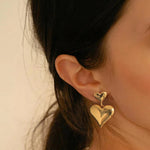Close-up of a woman wearing 18K gold plated double puffy heart statement drop earrings.