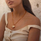 A woman wearing a beige off-the-shoulder top styled with an 18K gold chunky chain necklace featuring a ribbed puffy heart and front toggle clasp.