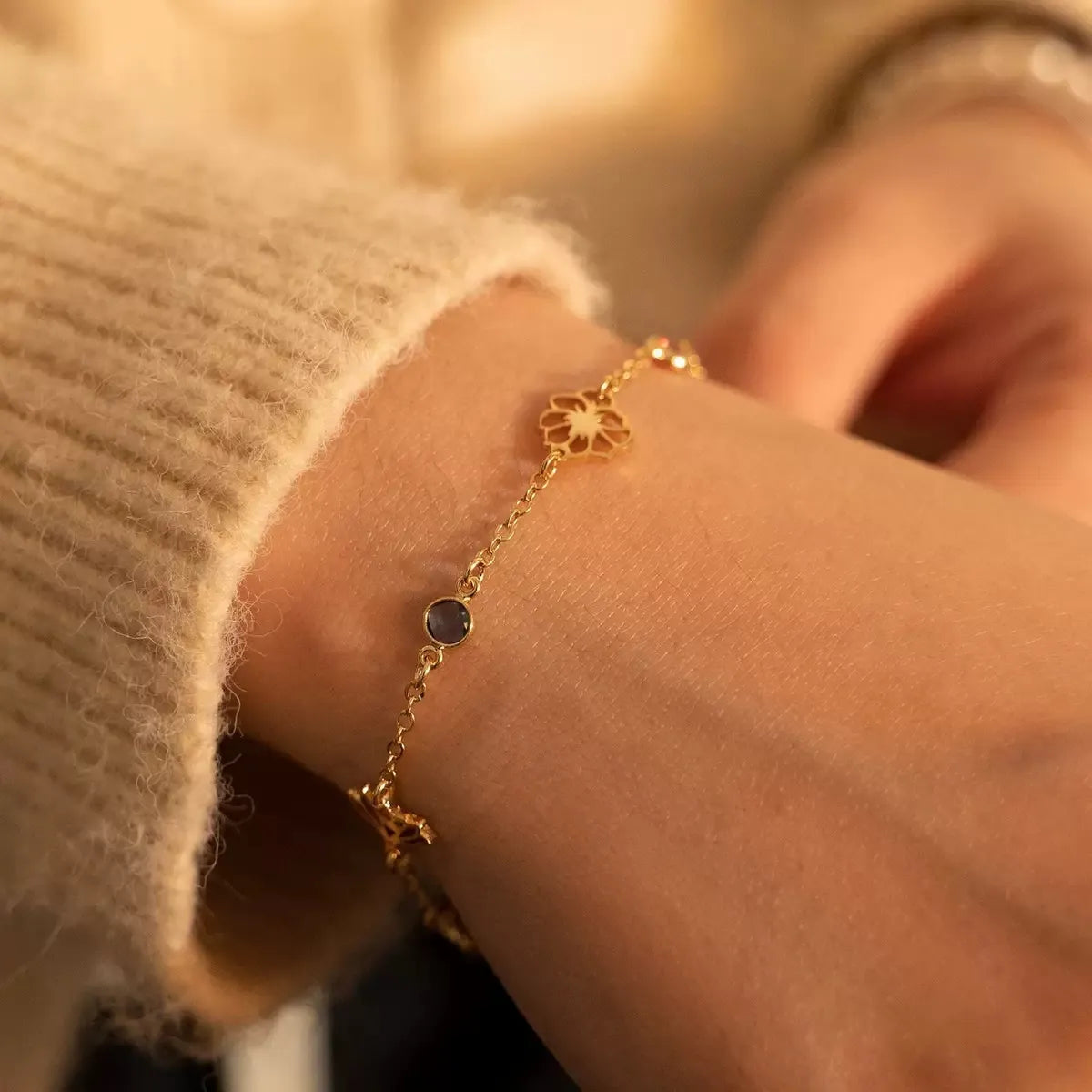 Close-up of a woman's wrist wearing a personalized gold birth flower and birthstone station bracelet.