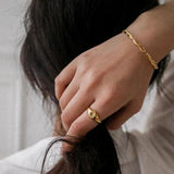 Close-up of a woman's hand touching the ends of her dark hair, wearing a dainty gold starburst signet ring without a stone on her pinky finger.