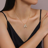 A model wearing a white top, showcasing the sparkly 18K gold plated moissanite bubble letter necklace on her collarbone.