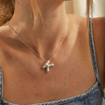 A woman wearing a high polish 925 sterling silver 3D puff initial letter K necklace on a delicate bean chain, styled with a blue denim top.