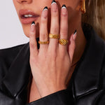 Close-up of a woman's hand with a French manicure resting near her face, modeling a chunky gold ribbed ring stacked alongside another twisted gold dome ring.