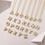 Three 18K gold plated moissanite bubble letter pendants lying flat next to a gold chain on a plain surface.