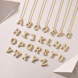 Three 18K gold plated moissanite bubble letter pendants lying flat next to a gold chain on a plain surface.