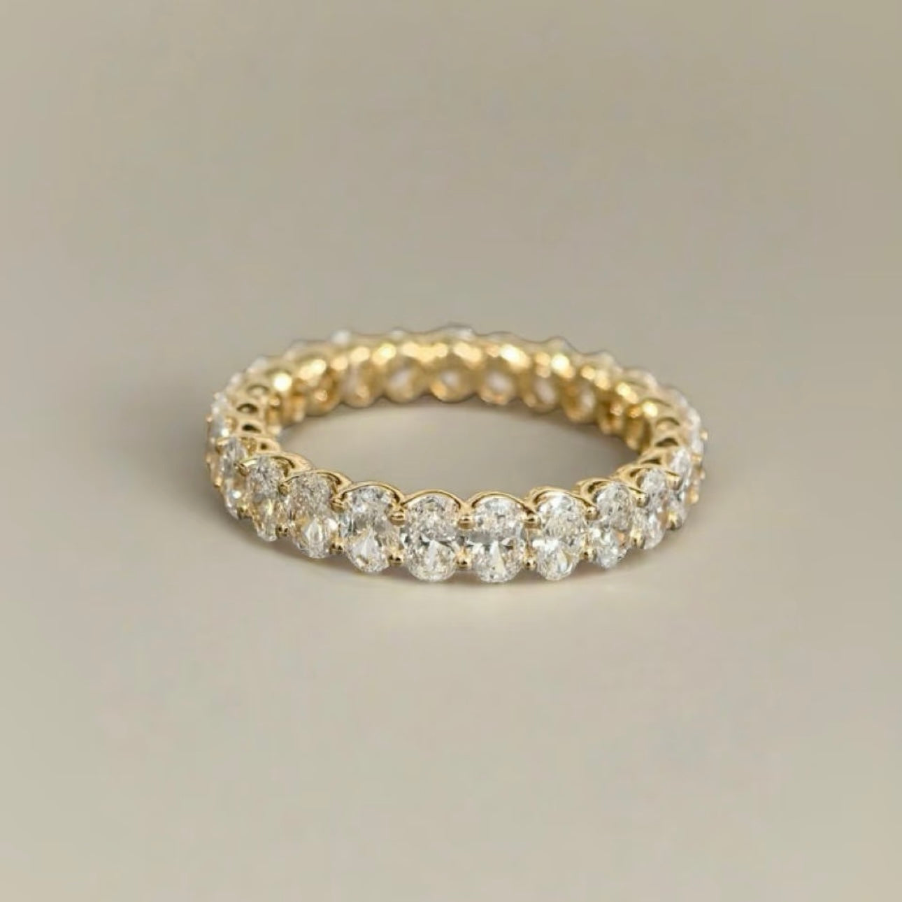 A close-up of the 18K gold Oval Lab Diamond Eternity Band standing upright against a soft white background, showcasing its uninterrupted sparkle.