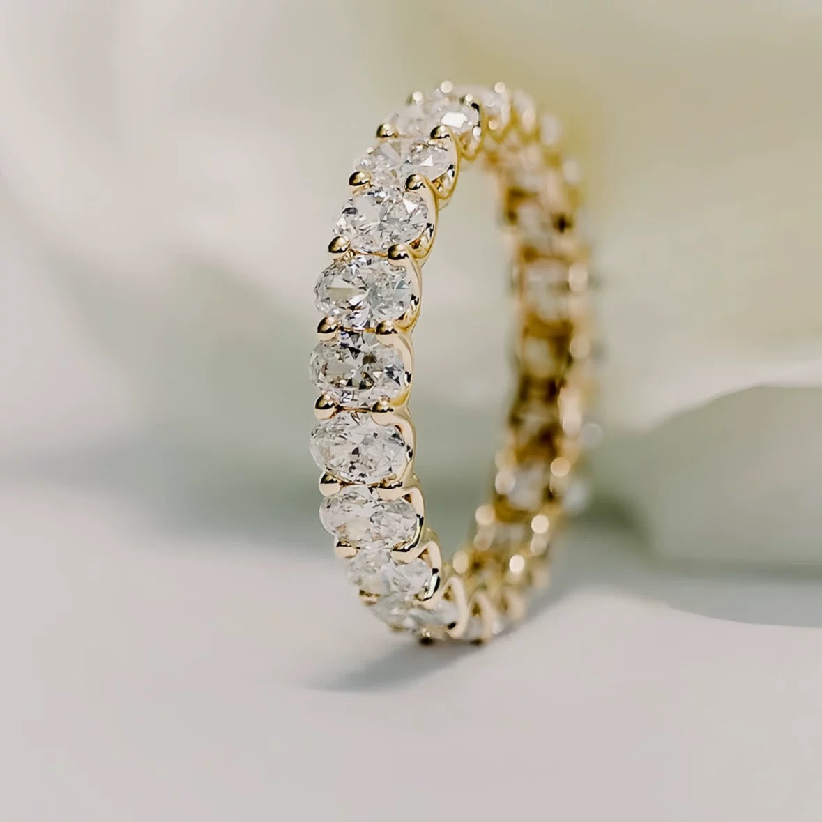 A close-up of the 18K gold Oval Lab Diamond Eternity Band standing upright against a soft white background, showcasing its uninterrupted sparkle.