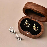 Wooden jewelry box with gold and silver 'KG' and 'KB' initials on a beige background