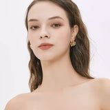 Portrait of a woman looking straight ahead with bare shoulders, showcasing a gold sculptural camellia flower earring.