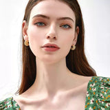 Portrait of a woman with blue eyes wearing a green floral top, showcasing a pair of chunky braided gold hoop earrings.