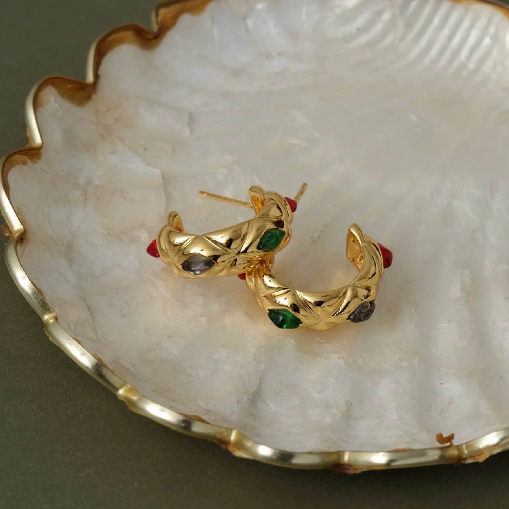 Retro-inspired quilted gold gemstone earrings resting on a white seashell for a luxury aesthetic.