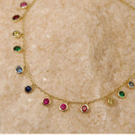 Close-up flat lay of the rainbow station necklace, highlighting the vibrant purple, blue, green, yellow, and pink CZ stones.