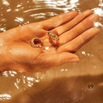 Aesthetic shot of the gemstone hoop earrings held in a hand over shimmering water, highlighting the gold's radiant shine.