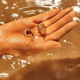 Aesthetic shot of the gemstone hoop earrings held in a hand over shimmering water, highlighting the gold's radiant shine.
