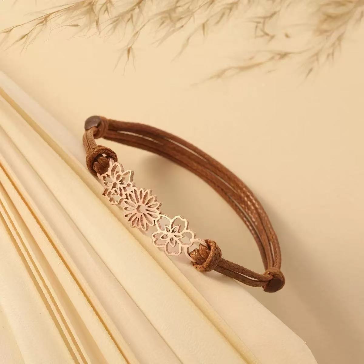 A delicate 18K rose gold personalized birth flower bracelet with three cutout charms resting on textured paper.