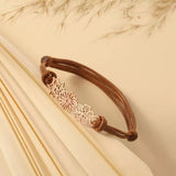 A delicate 18K rose gold personalized birth flower bracelet with three cutout charms resting on textured paper.