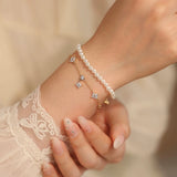 A woman wearing a delicate 14K rose gold plated clover charm bracelet stacked elegantly with a classic pearl bracelet.
