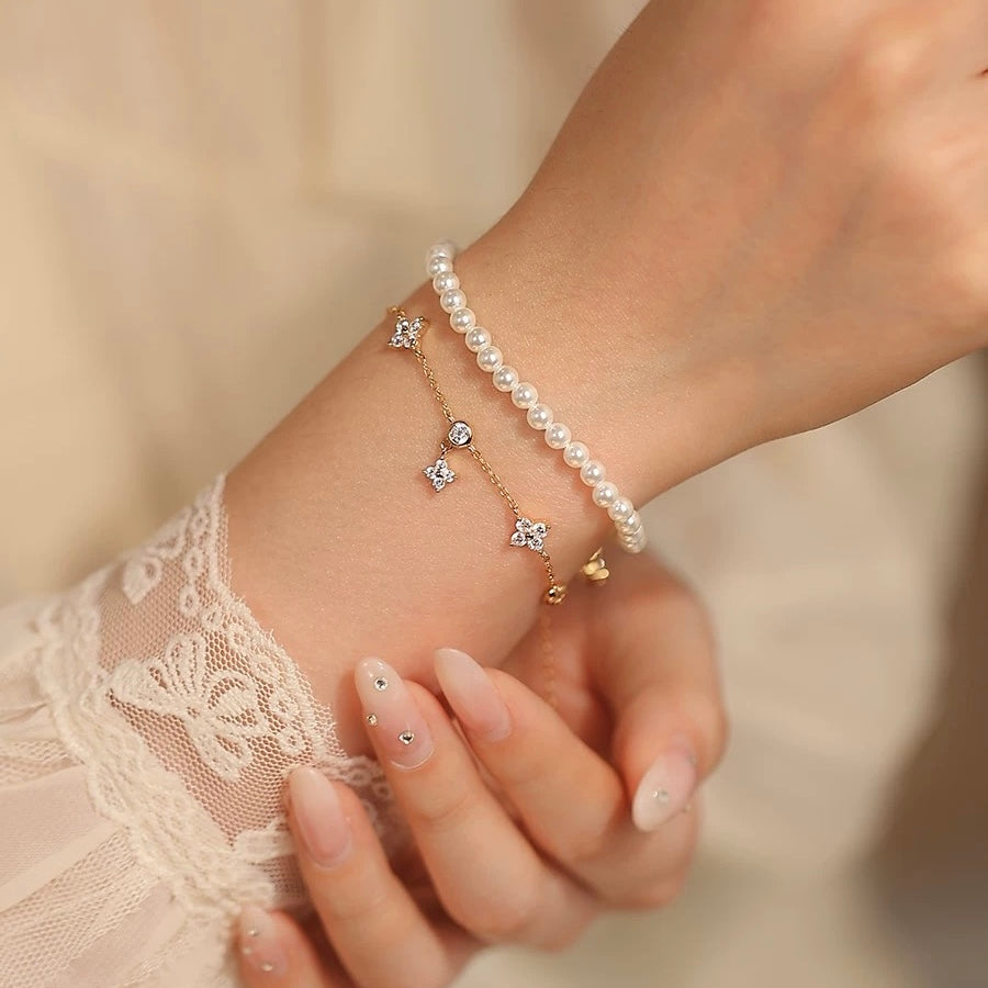 A woman wearing a delicate 14K rose gold plated clover charm bracelet stacked elegantly with a classic pearl bracelet.