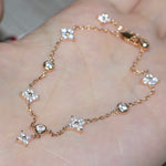 Close-up of a 14K rose gold plated clover charm bracelet resting on a palm, showing the sparkling micro-pave gemstone details.