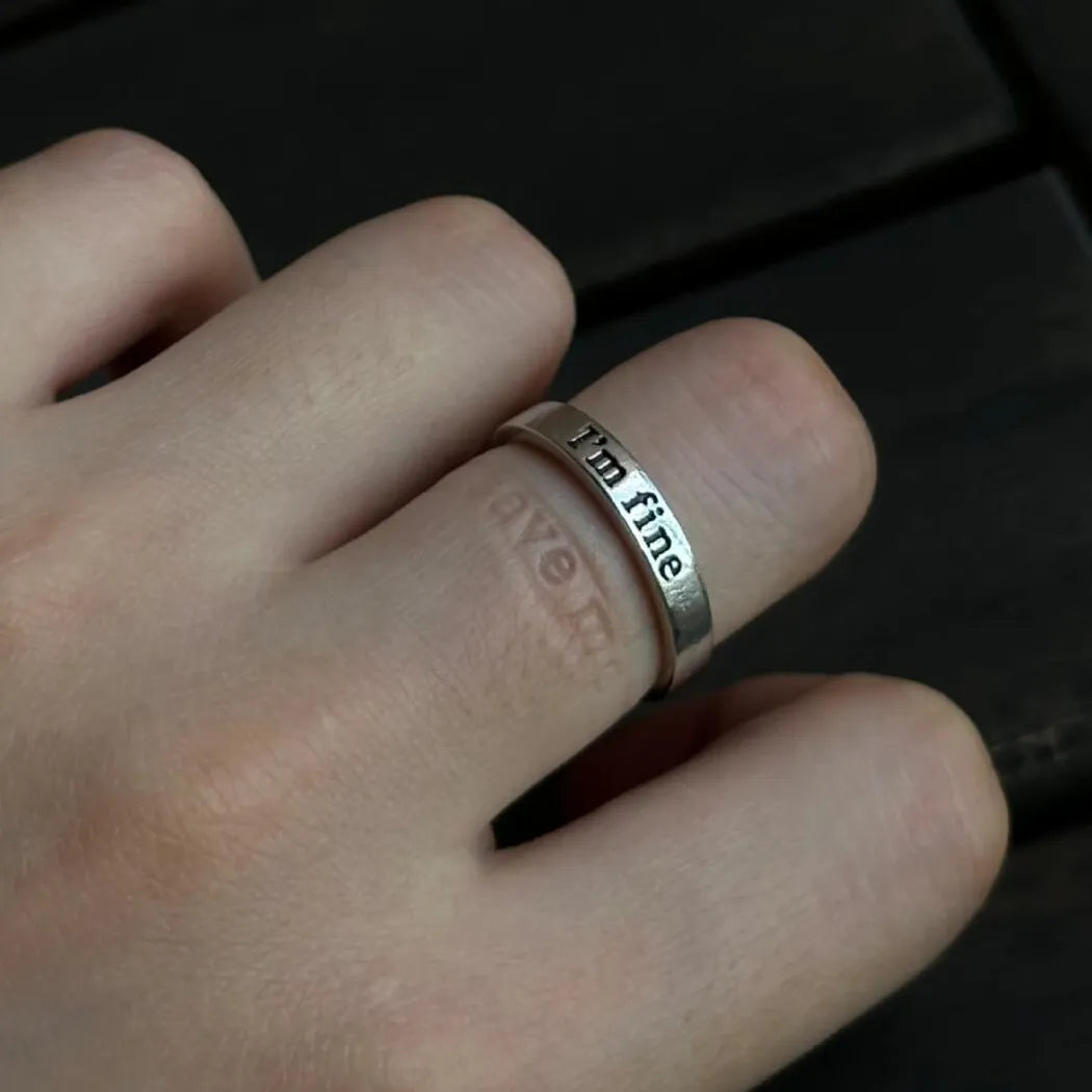 A silver "I'm fine" ring worn on a finger, with the hidden inside engraving leaving a faint, symbolic "save me" imprint on the skin.