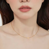 Close-up of a woman wearing the dainty 18K gold plated scattered hearts station necklace on her collarbone.