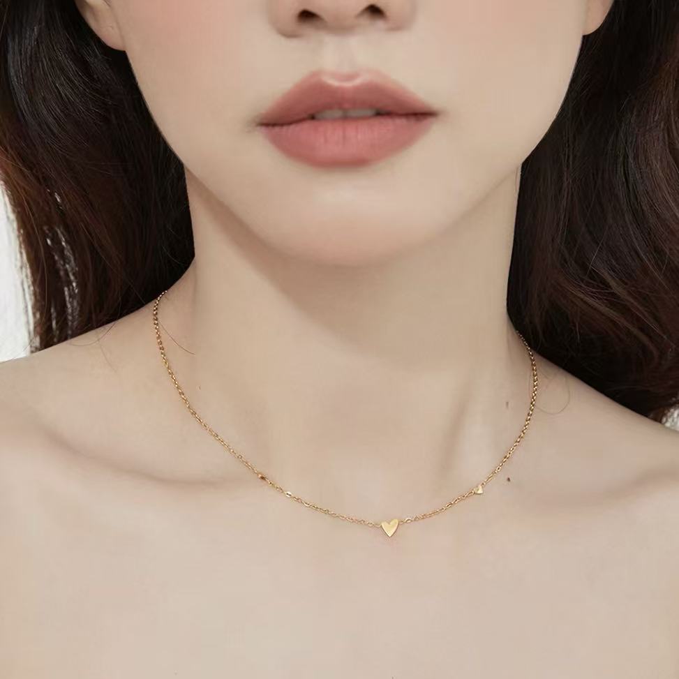 Close-up of a woman wearing the dainty 18K gold plated scattered hearts station necklace on her collarbone.