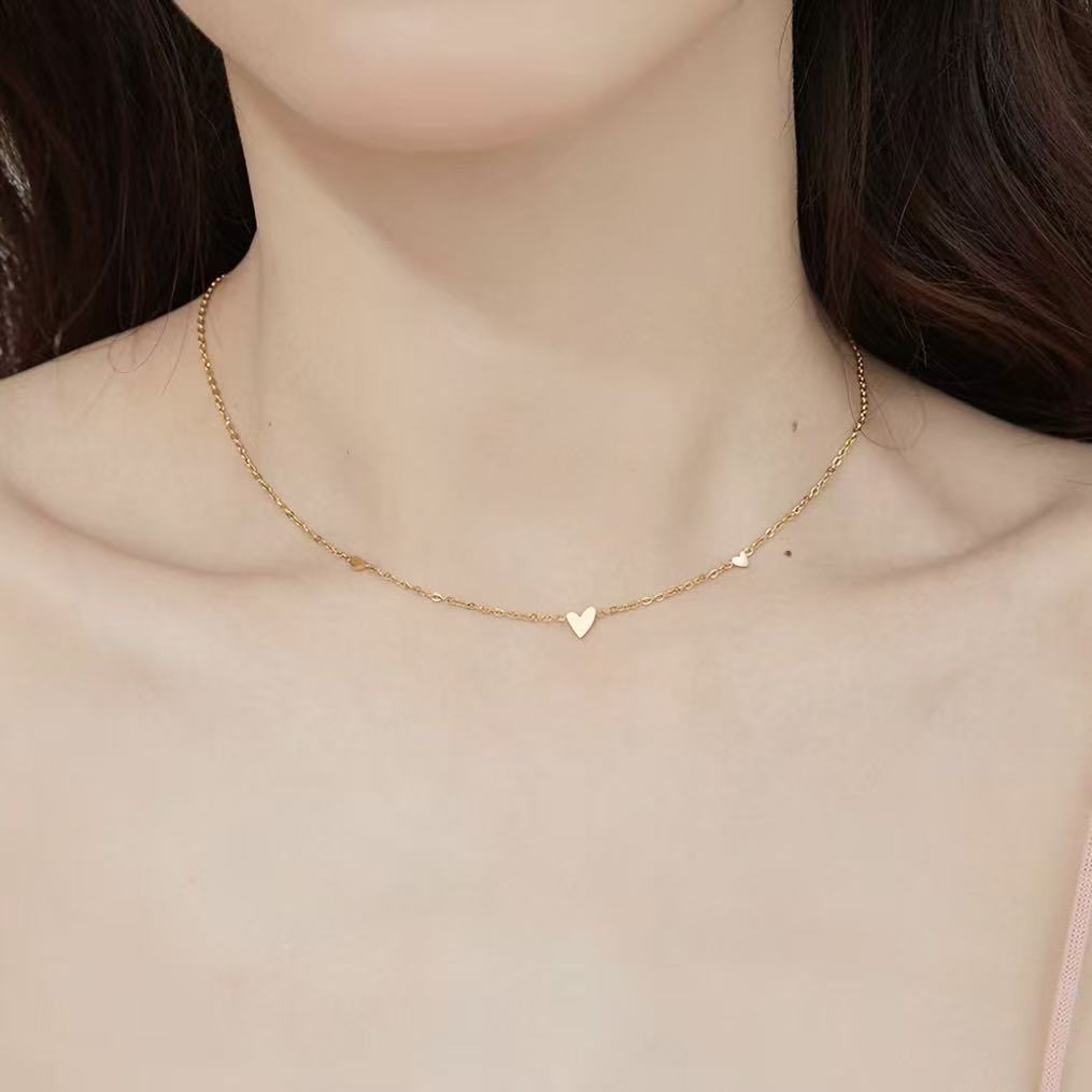 Close-up of a woman wearing the dainty 18K gold plated scattered hearts station necklace on her collarbone.