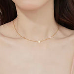 Close-up of a woman wearing the dainty 18K gold plated scattered hearts station necklace on her collarbone.