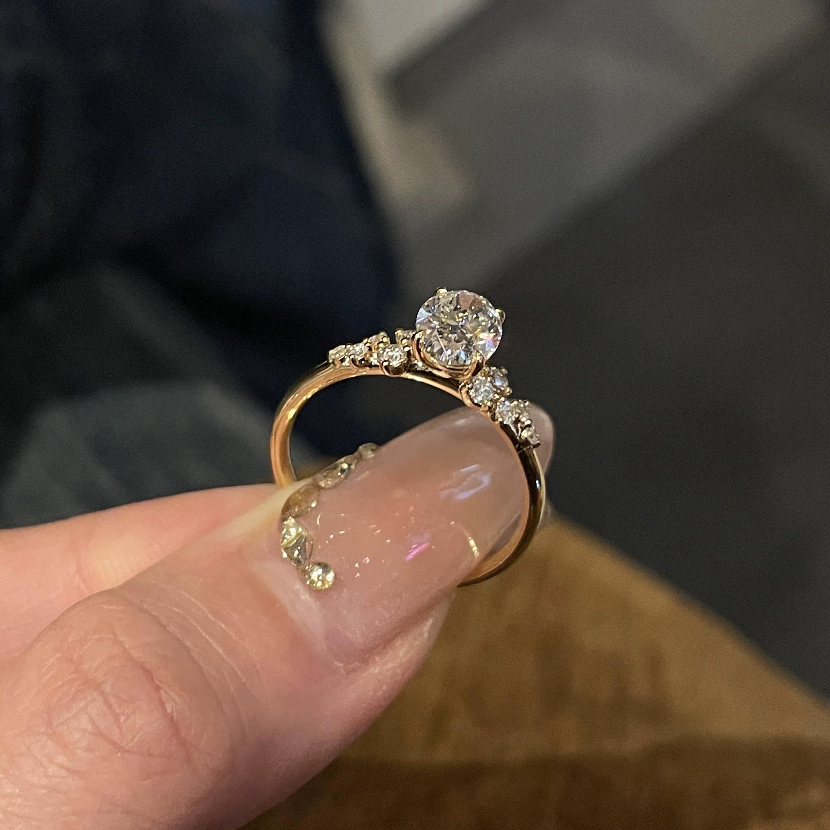 A hand holding the 18K gold Shooting Star Spark ring, showcasing the light-catching shared-prong halo setting.