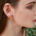 Side profile of a woman showing her ear adorned with a thick gold twisted rope hoop earring, wearing a green floral top.